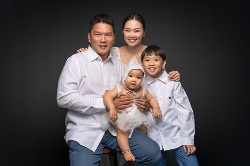 Happy family of four smiling at the camera in a Singapore portrait studio